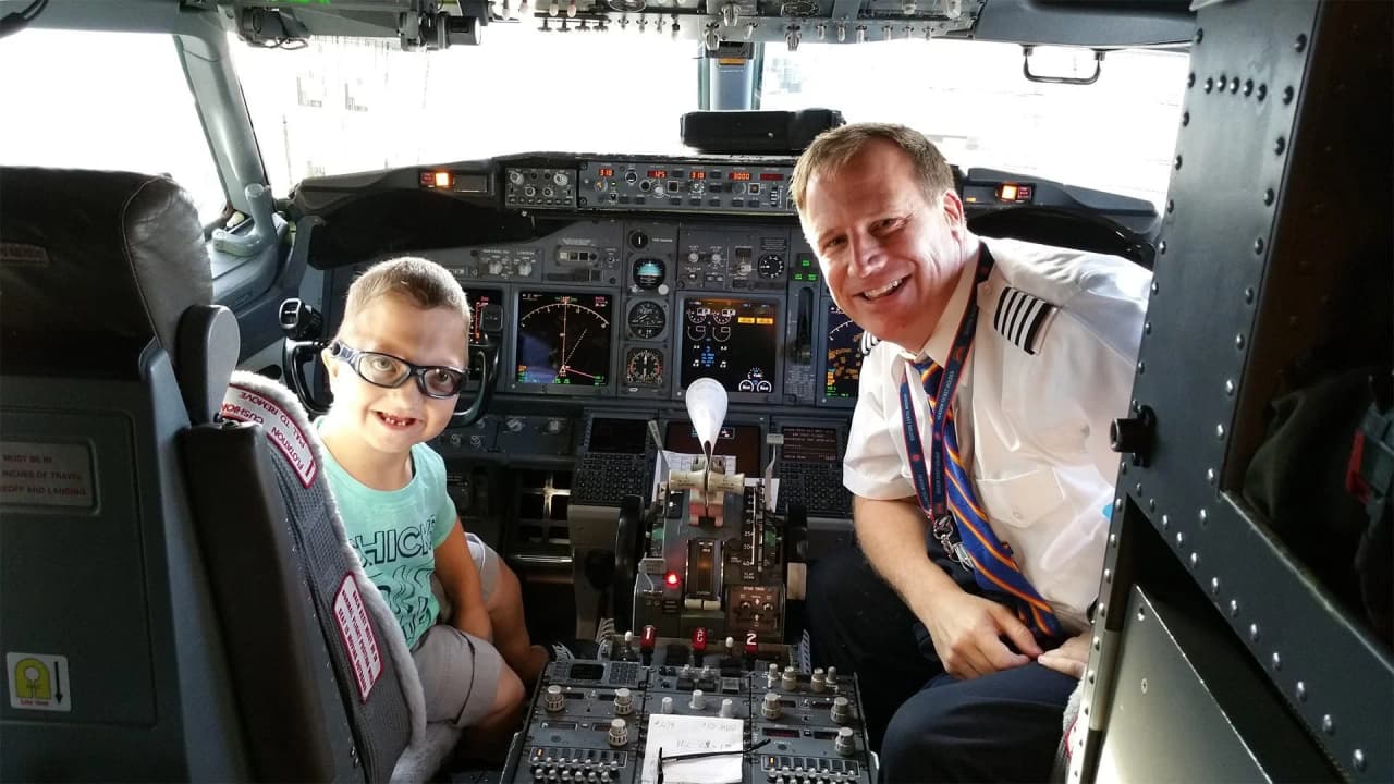 Child sitting in a cockpit with a smiling commercial pilot