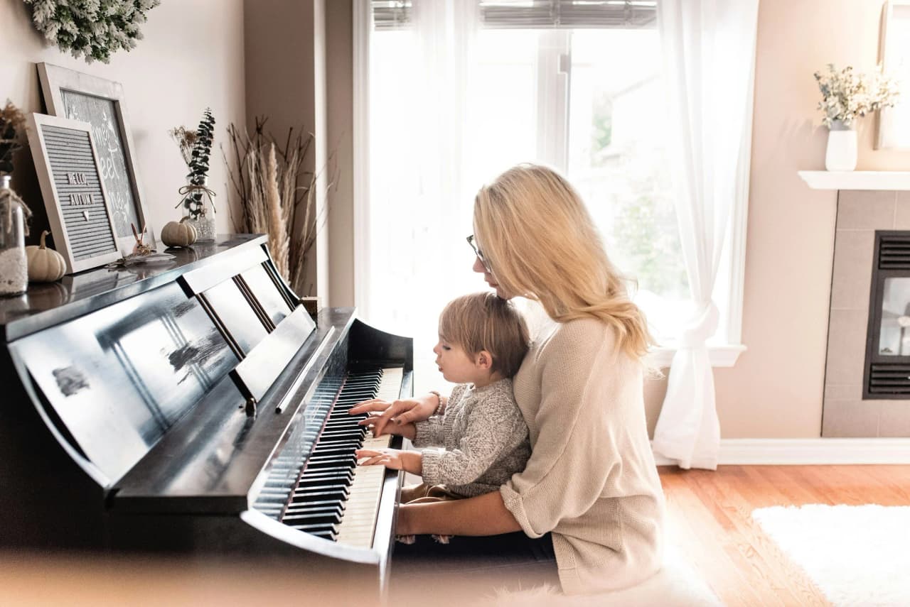 Adult and toddler sitting together at a piano in a living room