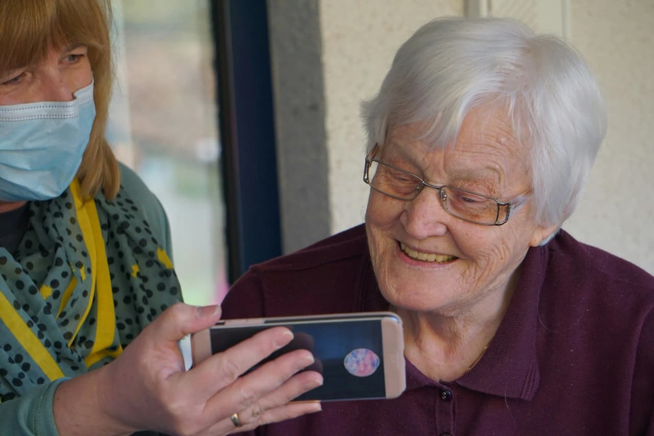 Caregiver and older woman smiling together while looking at a phone